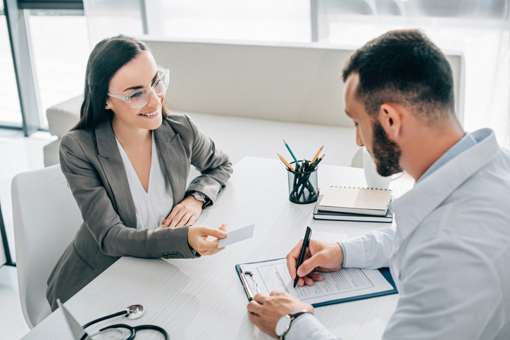 Man signing papers while a woman in suit gives him a card